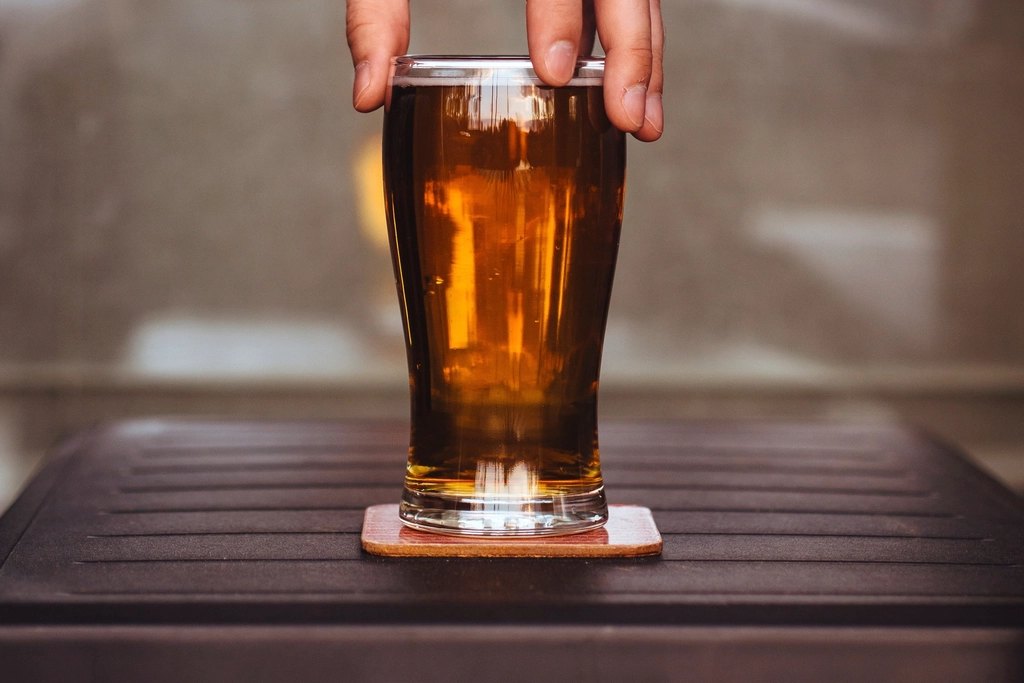 Mano con un vaso de cerveza sobre la mesa